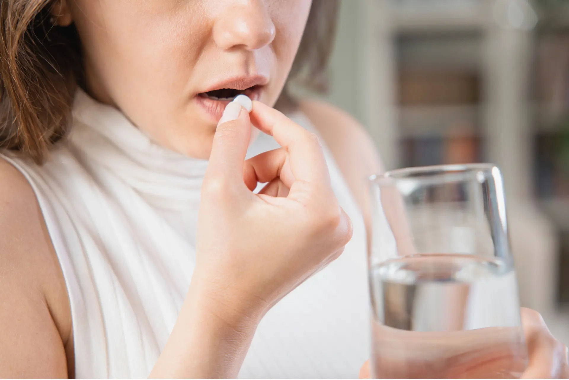 Person nimmt eine weiße Tablette mit einem Glas Wasser ein